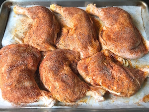 Chicken leg quarters seasoned on baking sheet.