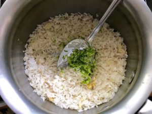 Adding lime zest to raw rice and garlic in pan.
