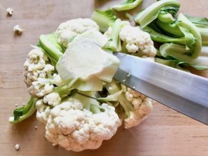 A head of cauliflower stem facing up, removing florets by tilting knife.