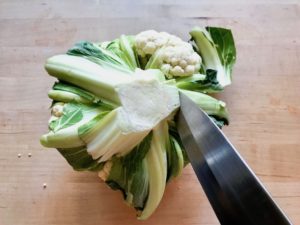 A head of cauliflower stem facing up, leaves being removed.