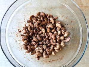 Tossing the roasted cashews with seasoning in a bowl.