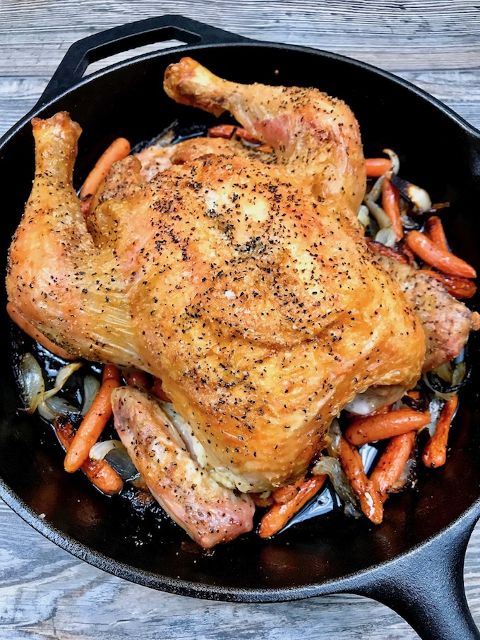 Simple Roast Chicken on top of caramelized onions and carrots in a skillet.