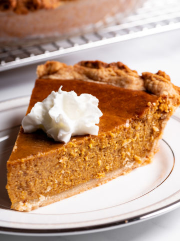 A slice of pumpkin pie with whipped cream on a white plate.