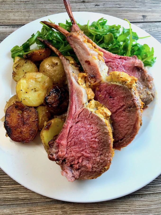 Three roasted lamb chops on a plate with roasted baby potatoes and arugula.