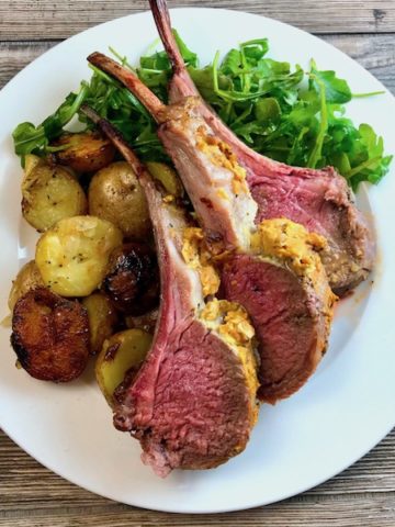 Three roasted lamb chops on a plate with roasted baby potatoes and arugula.