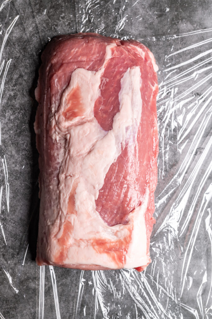 A boneless pork loin on plastic wrap.