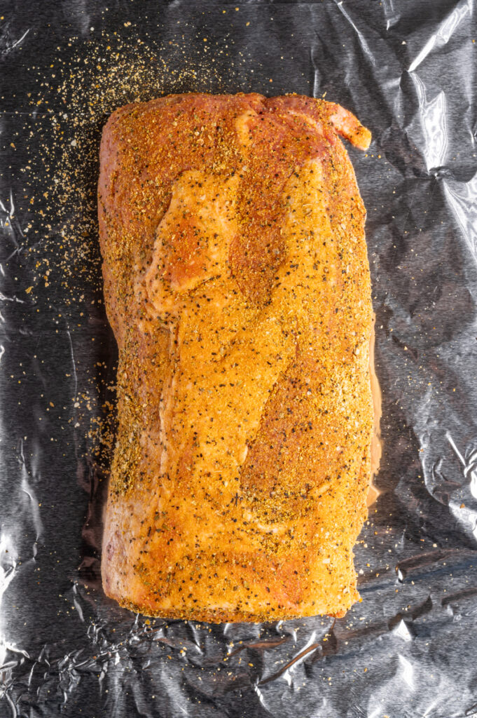 A pork loin seasoned with adobo seasoning on a foil-lined baking sheet.