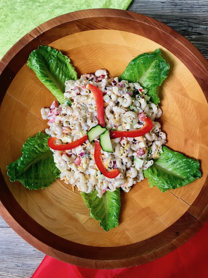 A bowl of macaroni salad garnished with red peppers and lettuce leaves.