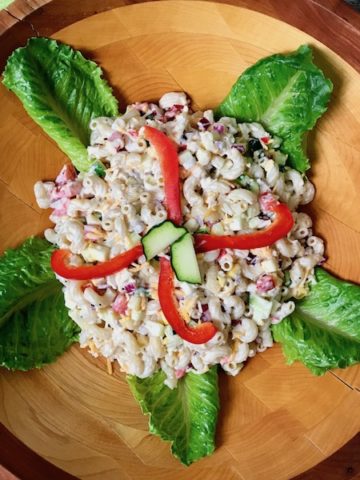 A bowl of macaroni salad garnished with red peppers and lettuce leaves.