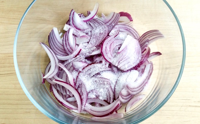 A bowl of sliced red onions sprinkled with kosher salt.