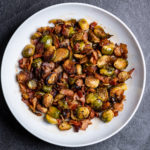 A white plate of roasted Brussels sprouts with bacon.