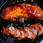 Oven baked bbq pork tenderloins in a skillet with one of them sliced.