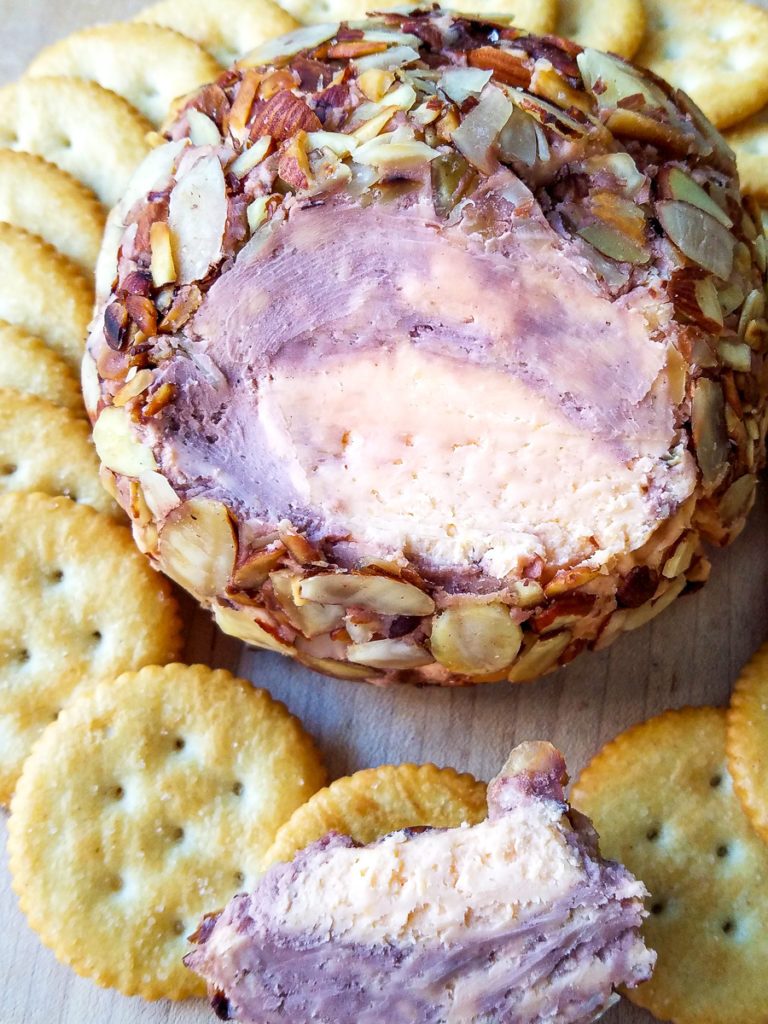 A port wine cheese ball with a piece scooped out on a cracker.