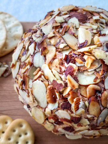 A port wine cheese ball coated in sliced almonds on a board.