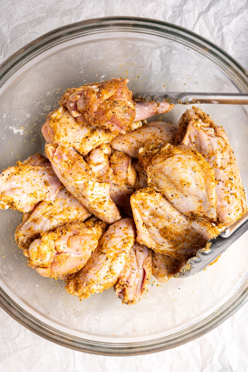 Chicken wings tossed with seasonings in a bowl.