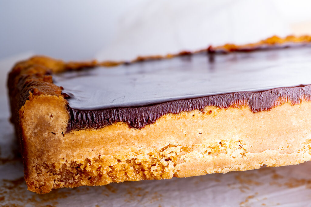 A side view of a peanut butter bar topped with chocolate ganache.