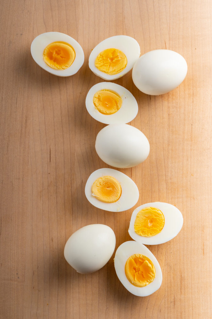 Boiled peeled eggs with some sliced on a board.