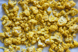 Curry cauliflower florets on sheet pan ready to bake.