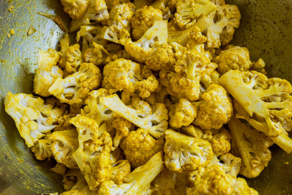 Cauliflower florets coated in curry spices in a bowl.