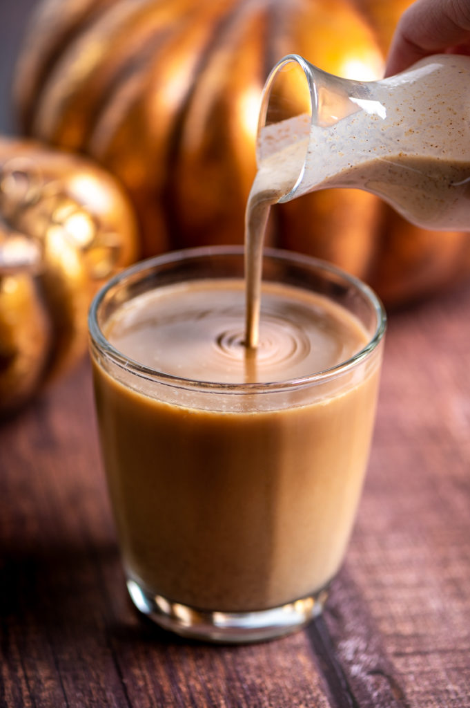Pumpkin spice creamer being poured into a cup of coffee.