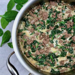 A skillet of ground beef with spinach and cream.