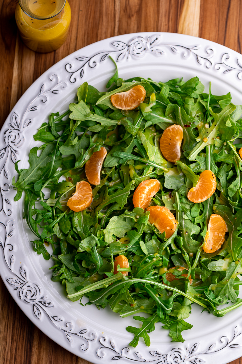 A white platter with arugula and clementines drizzled with orange vinaigrette.