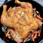 Simple Roast Chicken on top of caramelized onions and carrots in a skillet.