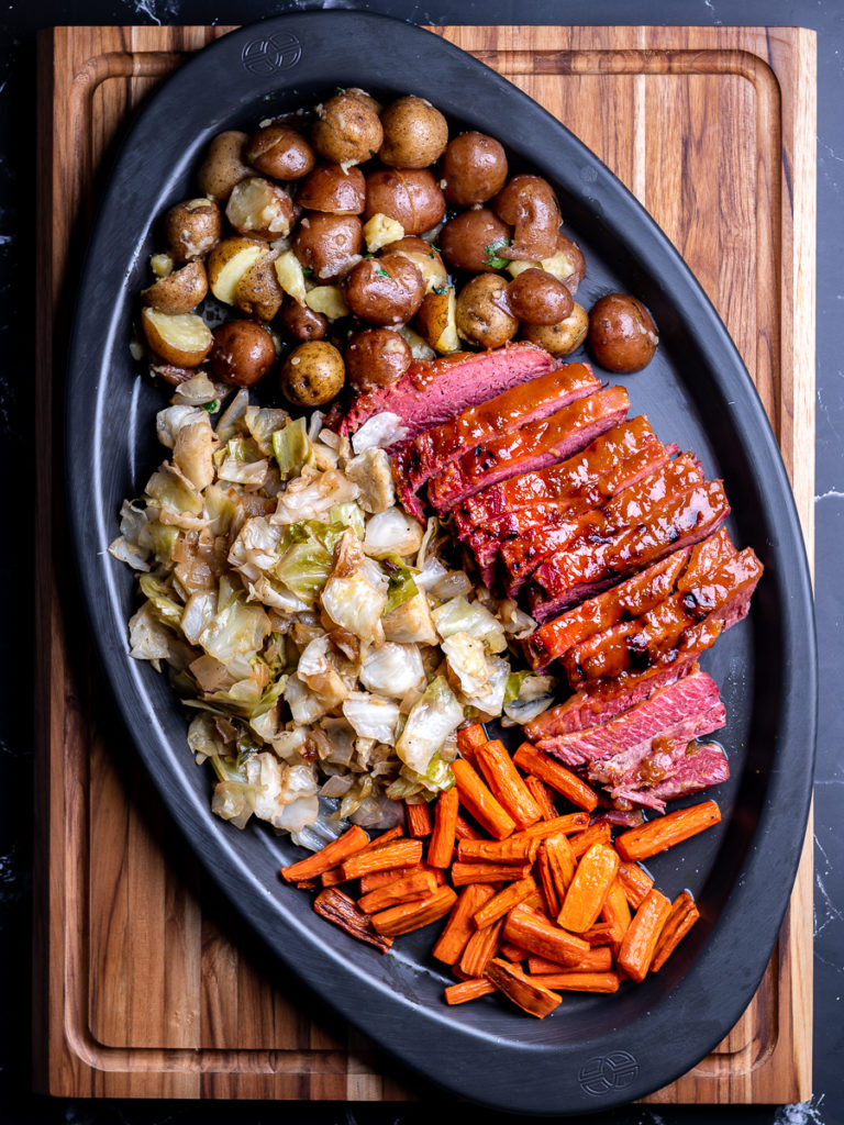 A black tray with sliced corned beef, baby potatoes, sautéed cabbage, and roasted carrots.