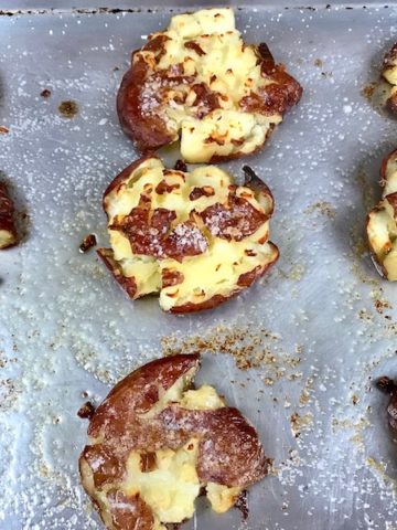 Golden smashed potatoes on a baking sheet.