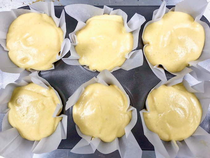 Corn muffin batter in a muffin tin lined with parchment paper liners.