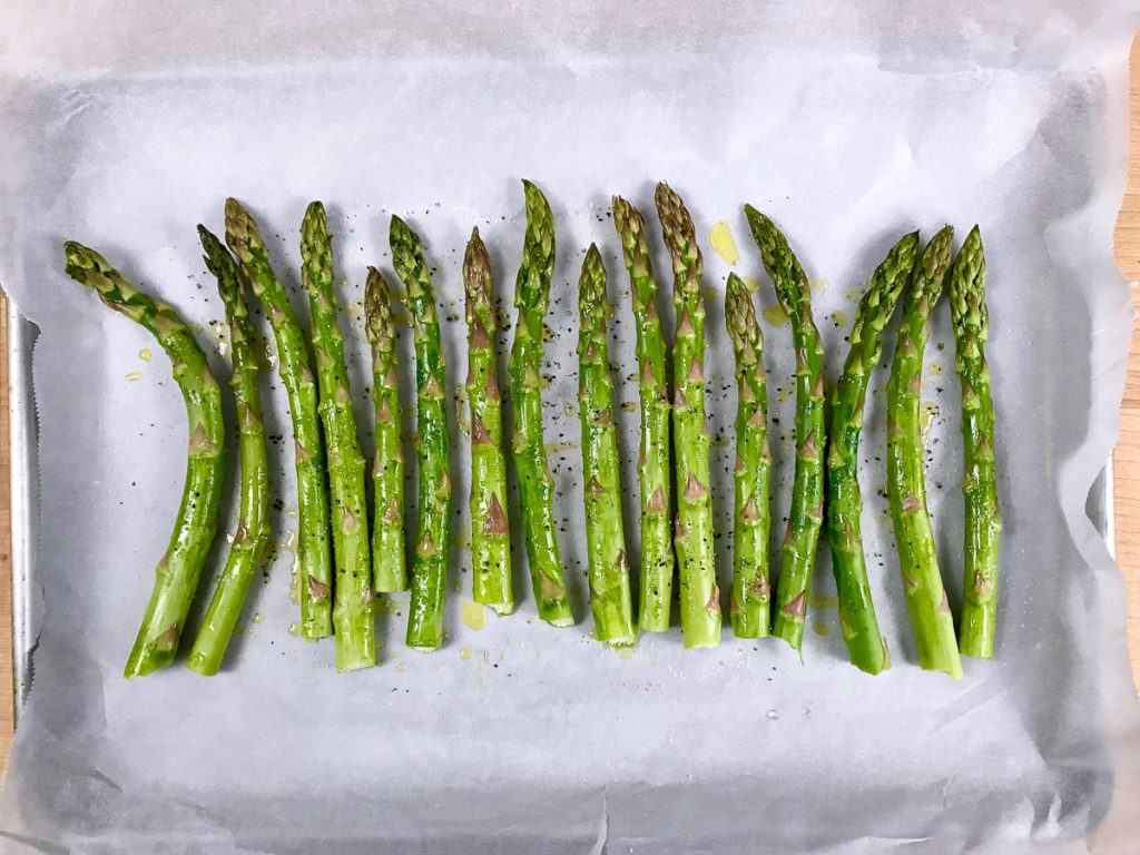 Asparagus coated with olive oil, salt, and pepper on a baking sheet.