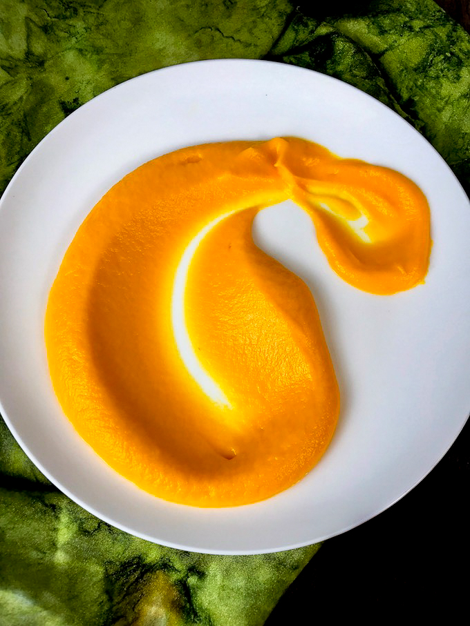 A spoonful of carrot puree spread out on a white plate.