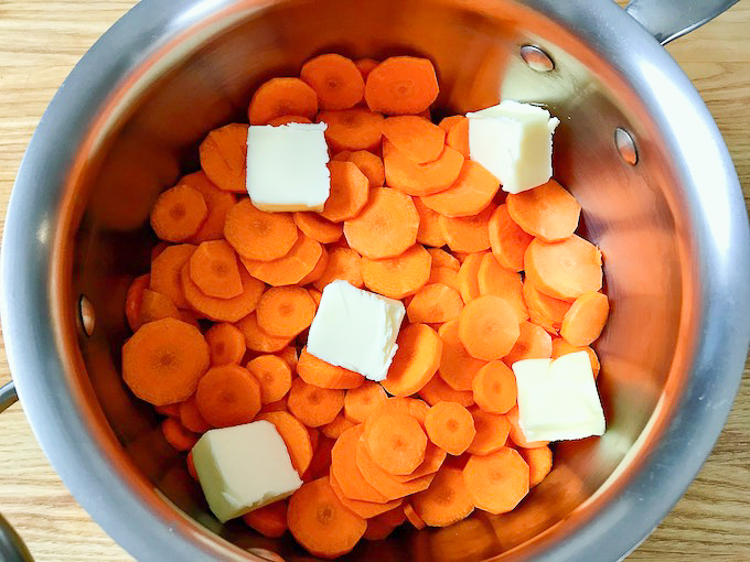 A saucepan filled with sliced carrots and butter.