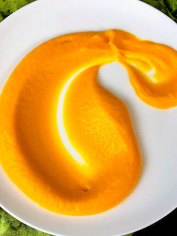 A spoonful of carrot puree spread out on a white plate.
