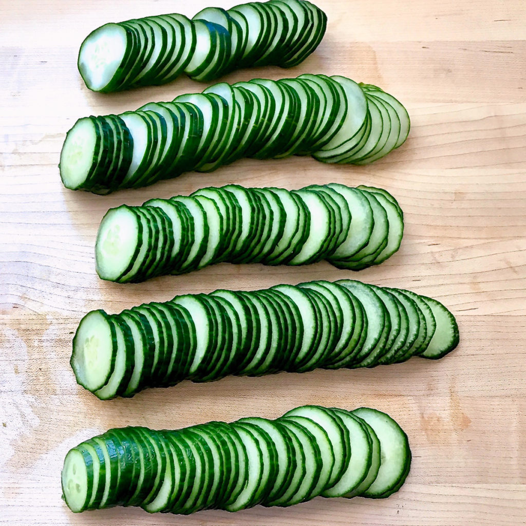Thinly sliced cucumbers on a cutting board.