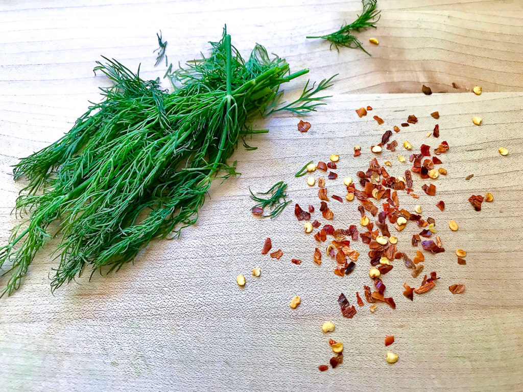 Fresh dill and crushed red pepper on a cutting board.
