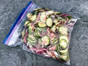 Sliced cumbers and red onions marinating in a zip top bag.