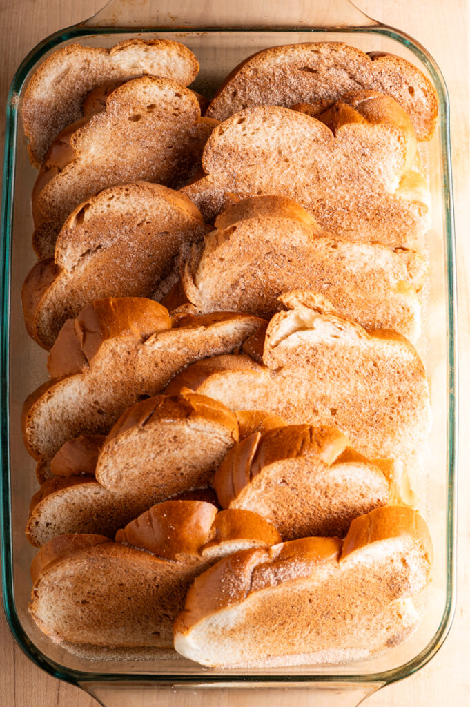 Slices of bread in a baking dish coated with cinnamon sugar.