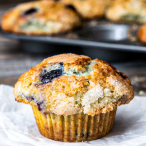 A blueberry muffin with a pan of muffins in the background.