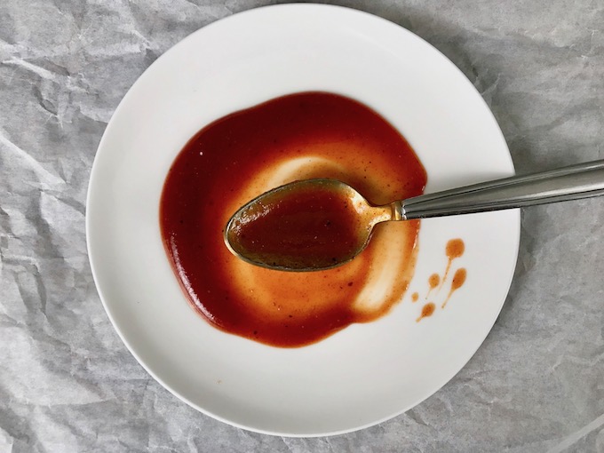 A white plate with a spoon of bbq sauce spread on it.