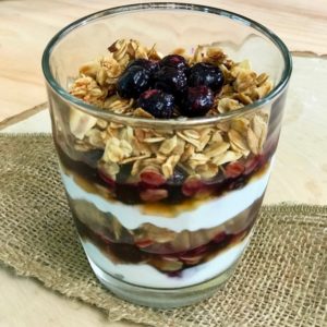 A glass of blueberry parfait showing layers of yogurt, blueberries, and granola.
