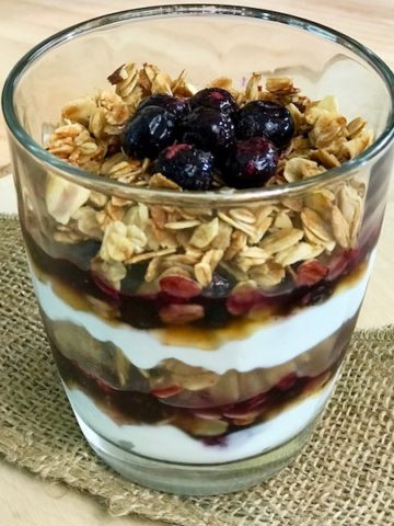 A glass of blueberry parfait showing layers of yogurt, blueberries, and granola.