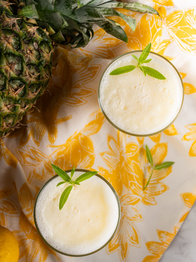 Two glasses of pineapple ginger lemonade with a pineapple in the background.