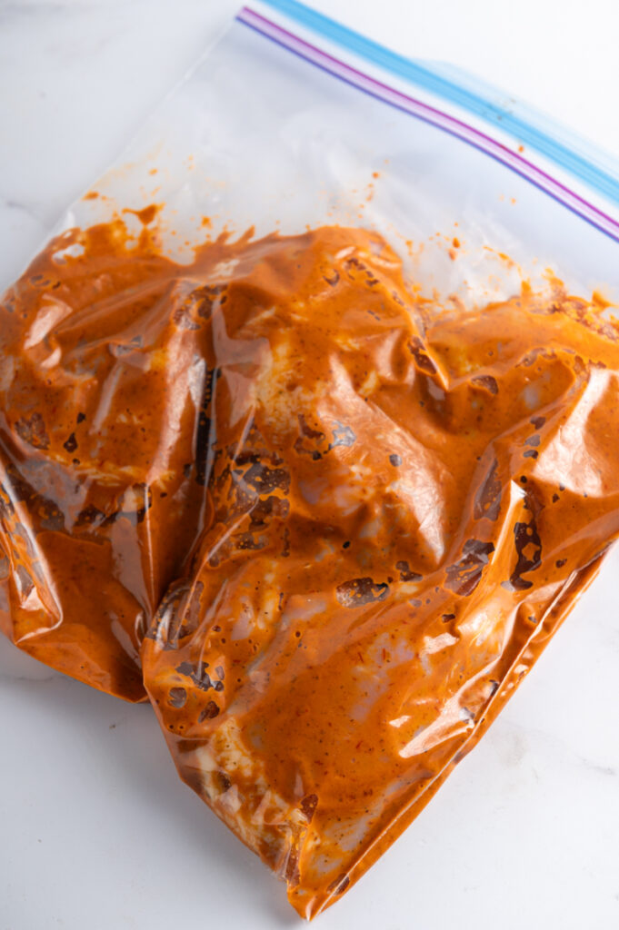 Chicken thighs marinating in a chipotle marinade in a zip top bag.