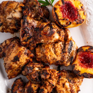 Chipotle chicken thighs on a platter with grilled peaches.
