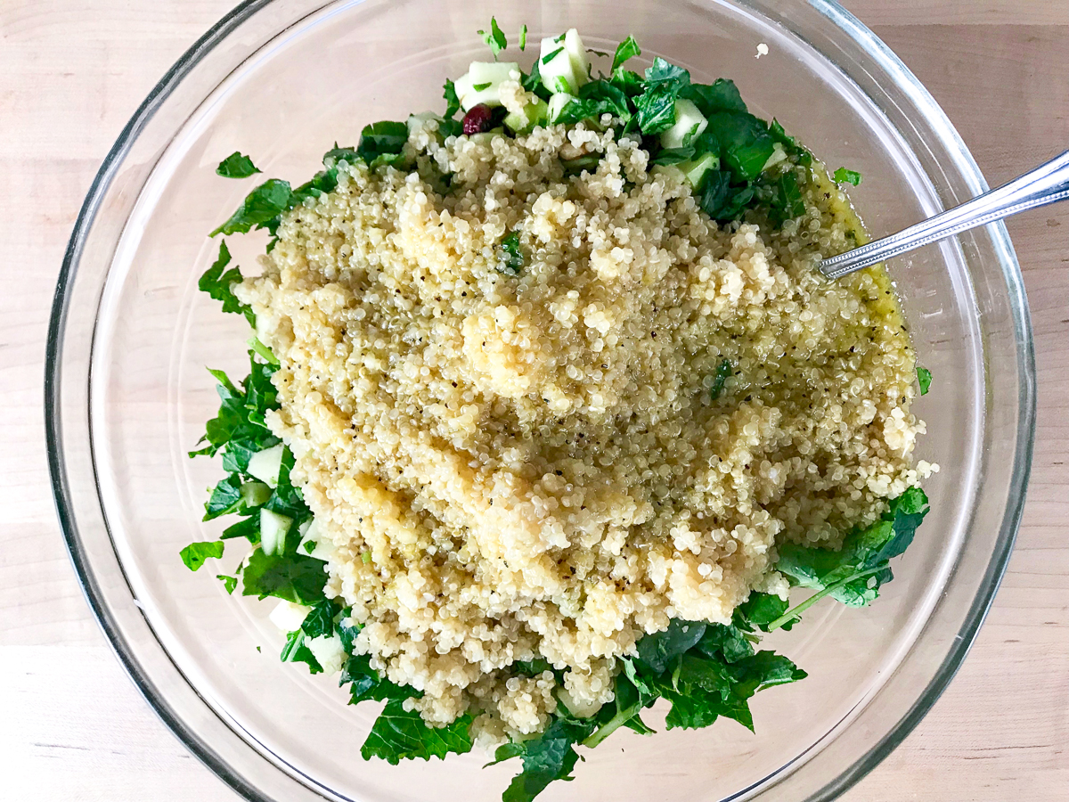 Quinoa is added to the kale in a bowl.