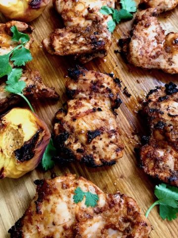 Grilled chipotle chicken with grilled peaches on a cutting board.