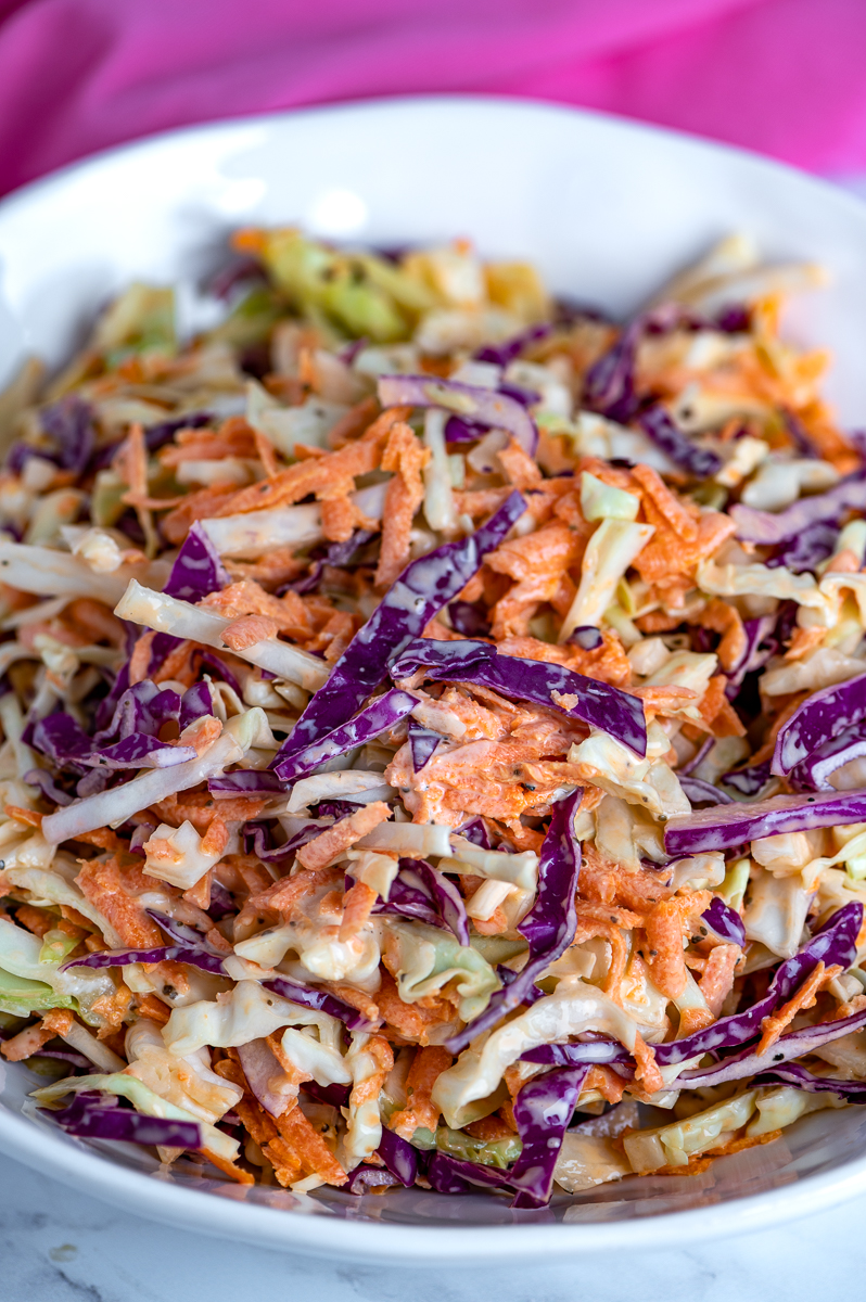 Shredded green and red cabbage with grated carrots coated with dressing in a white bowl.