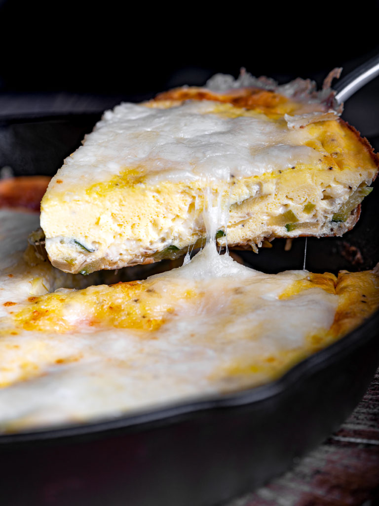 A slice of zucchini frittata being lifted from skillet.