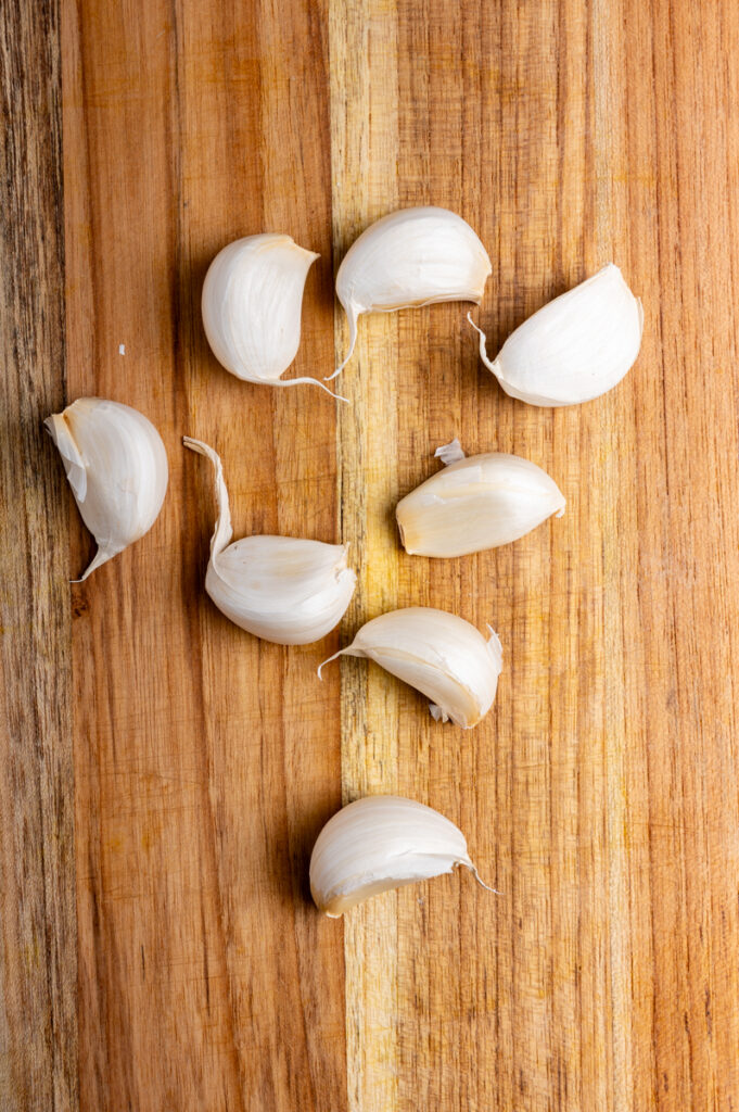 Eight cloves of garlic scattered on a cutting board.